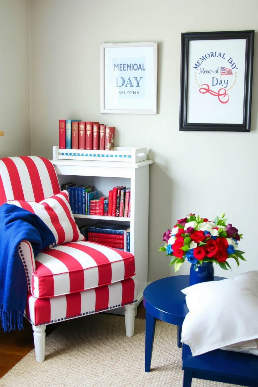 A cozy reading nook features a red and white striped armchair with a blue throw blanket draped over the side. A small bookshelf painted in white holds an array of books with red and blue covers, creating a patriotic display. On the wall, a framed art piece with a Memorial Day theme adds a festive touch. A small side table in a deep blue hue holds a vase of fresh flowers in red, white, and blue, enhancing the overall theme of the space.