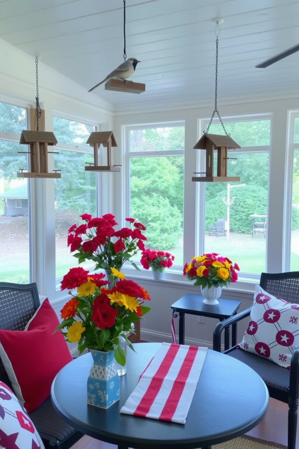 Charming bird feeders made from reclaimed wood are scattered throughout the sunroom creating a cozy atmosphere. Each feeder is designed to attract a variety of birds, enhancing the natural beauty of the space. For Memorial Day, the sunroom is adorned with red, white, and blue accents including patriotic throw pillows and table runners. Fresh flowers in vibrant colors are placed on the windowsills, bringing a festive touch to the serene environment.