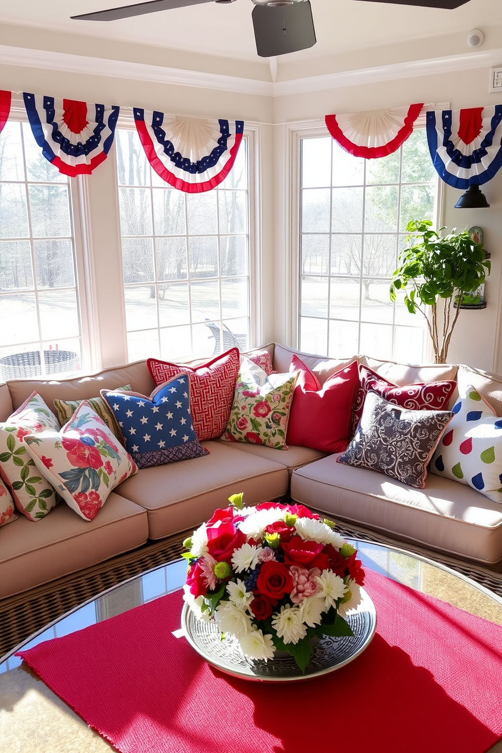 Colorful throw pillows in various shapes and sizes are arranged on a comfortable sectional sofa, adding a vibrant touch to the sunroom. The pillows feature a mix of floral and geometric patterns, complementing the natural light streaming in through large windows. For Memorial Day, the sunroom is adorned with red, white, and blue accents, including a festive table centerpiece made of fresh flowers. Patriotic banners hang from the ceiling, creating a cheerful atmosphere for gatherings and celebrations.