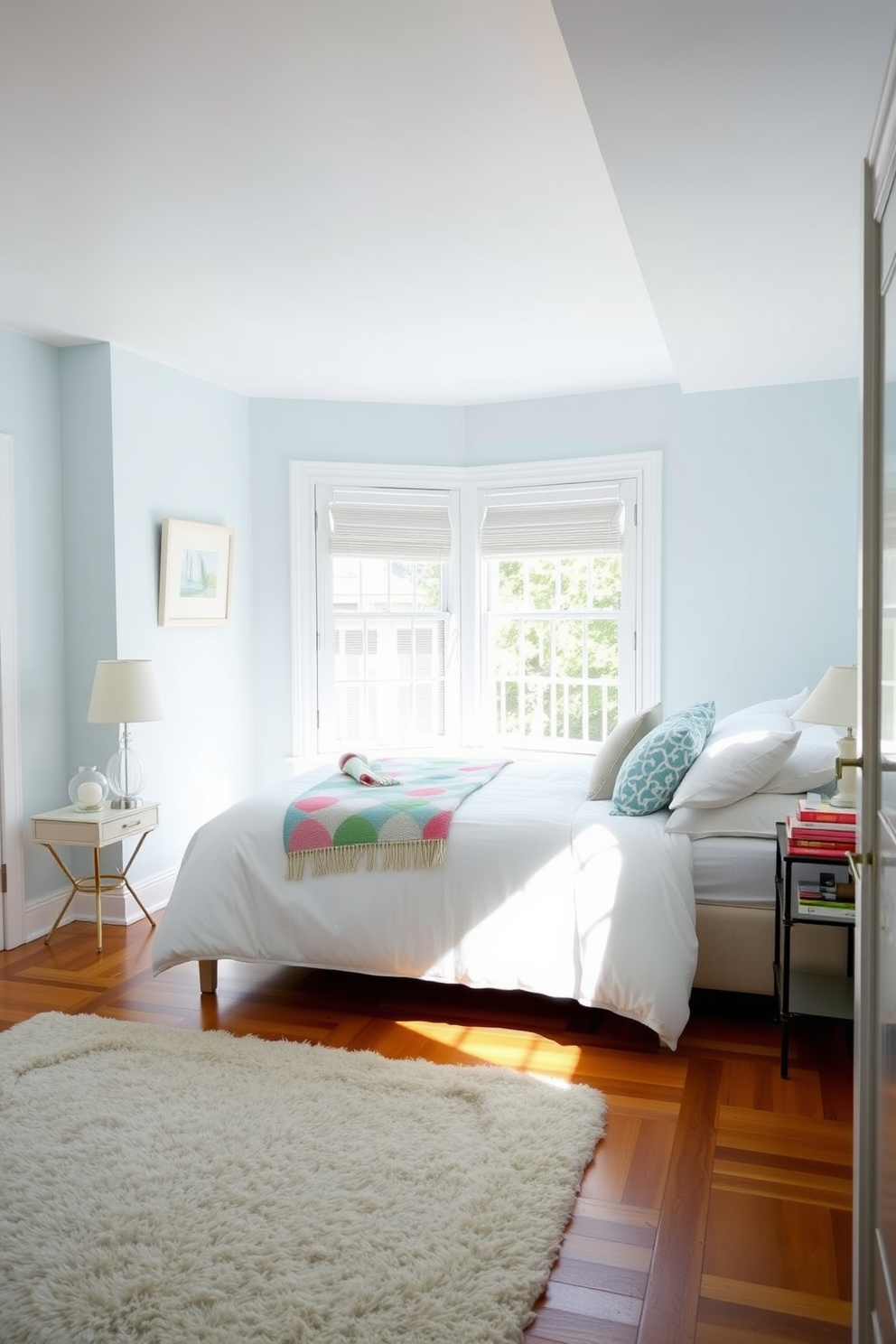 A bright and airy bedroom adorned with soft pastel colors. A large window lets in natural light, illuminating the space where a cozy bed is dressed in crisp white linens and topped with a colorful throw blanket. On one side of the bed, a stylish nightstand holds a small lamp and a stack of books. The walls are painted in a soothing light blue, while a plush area rug adds warmth to the hardwood floor.