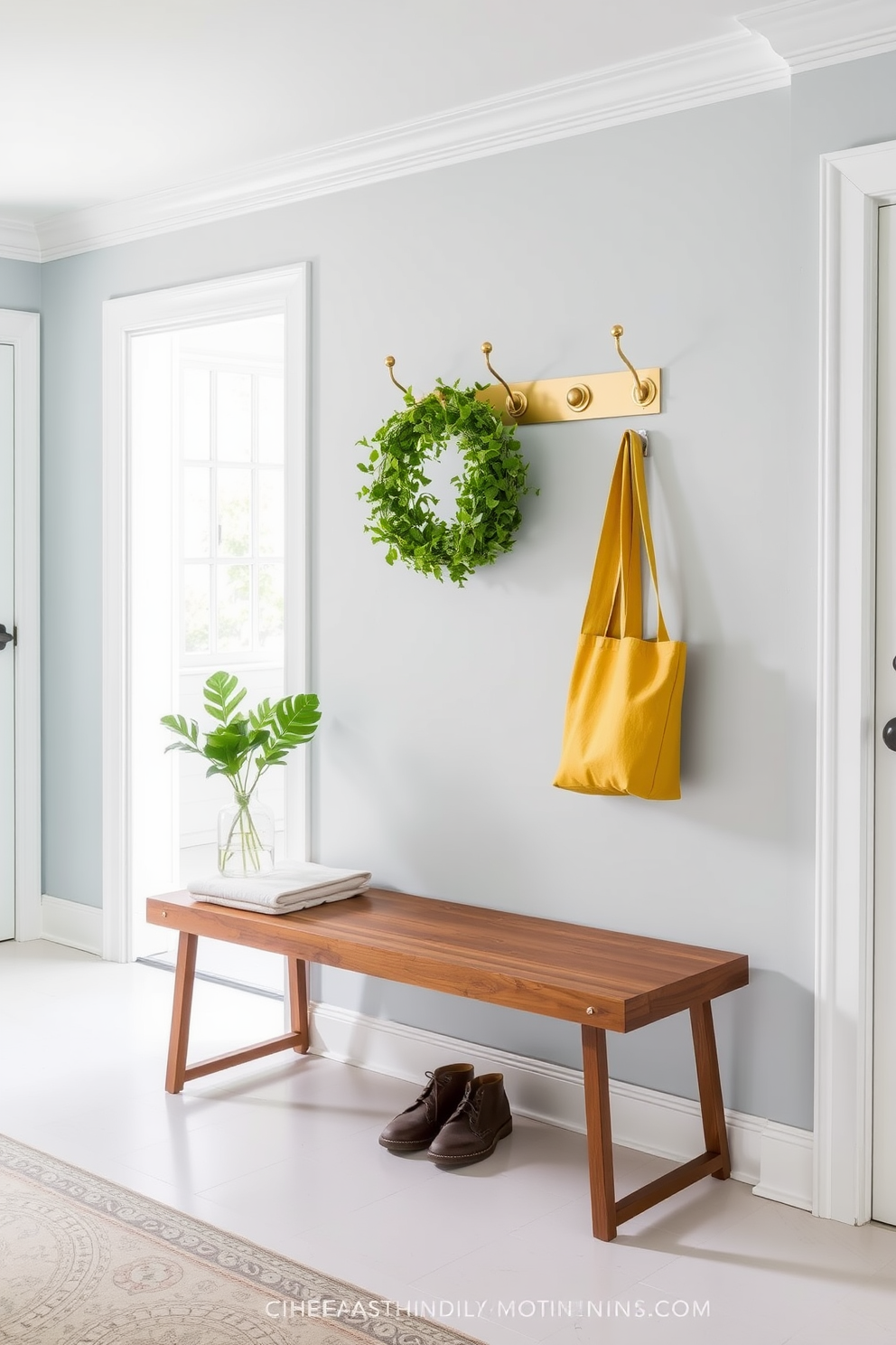 A bright and welcoming entryway features wall-mounted hooks made of brushed brass for stylish organization. Beneath the hooks, a sleek wooden bench with a soft cushion provides a perfect spot to sit while putting on shoes.