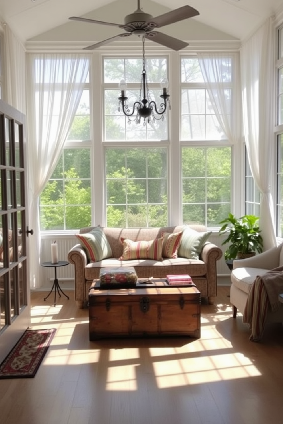 A bright and airy sunroom filled with natural light. There are large windows adorned with sheer white curtains, allowing the summer sun to stream in. In the center, a comfortable seating area features a plush sofa with colorful throw pillows. A vintage trunk sits at the foot of the sofa, providing stylish storage for blankets and games.