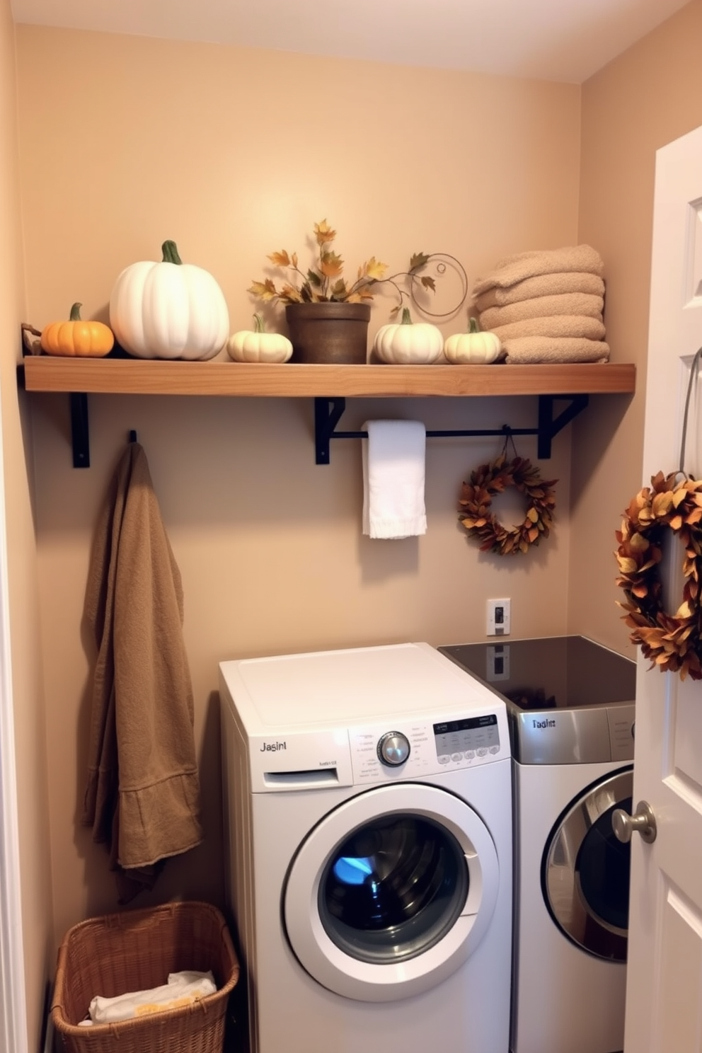 A cozy laundry room adorned with pumpkin decor accents on the shelves creates a festive atmosphere. Soft orange and cream pumpkins are artfully arranged alongside neatly folded towels and laundry supplies. The walls are painted in a warm beige tone, enhancing the welcoming feel of the space. A rustic wooden shelf holds seasonal decorations, while a small wreath made of autumn leaves hangs on the door.