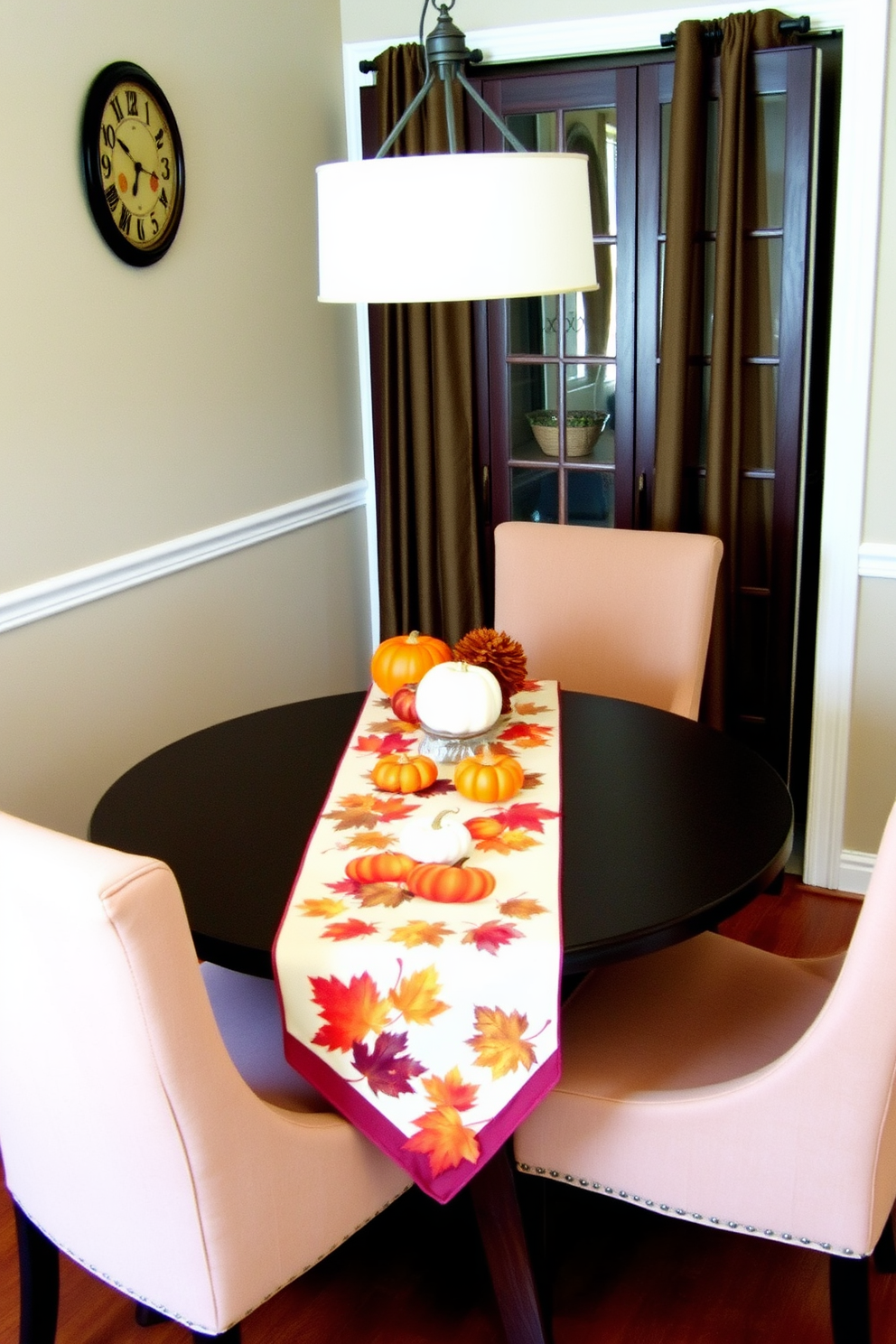 A cozy dining area featuring a small round table adorned with a Thanksgiving-themed table runner. The runner is decorated with autumn leaves and pumpkins, creating a warm and inviting atmosphere for family gatherings. Around the table, there are four upholstered chairs in earthy tones that complement the seasonal decor. Soft lighting from a nearby pendant lamp enhances the intimate setting, making it perfect for a festive meal.