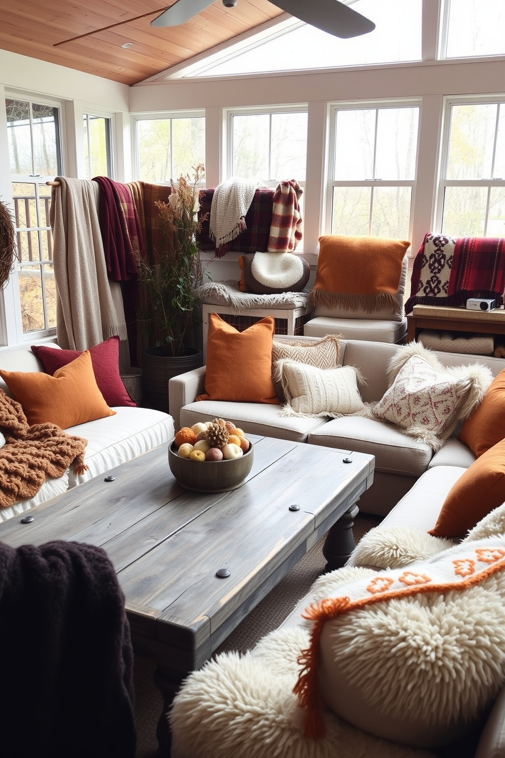 A cozy sunroom filled with layered textures featuring various blankets and pillows in warm autumn colors. The space is adorned with a rustic wooden coffee table surrounded by plush seating, inviting relaxation and conversation.