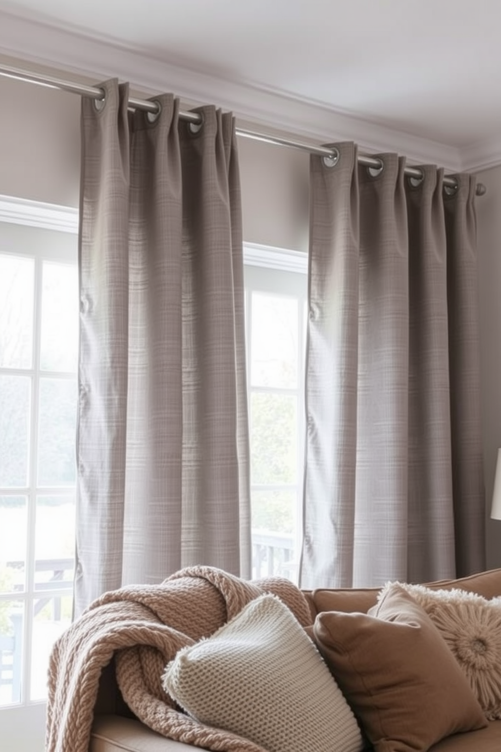 Textured curtains in a soft gray fabric drape elegantly from a sleek curtain rod, creating a cozy atmosphere while effectively blocking drafts. The curtains complement a warm color palette in the room, enhancing the winter decor with layered blankets and plush pillows on the sofa.