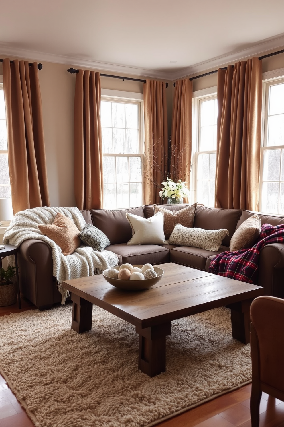 A warm and inviting living room adorned with soft, cozy textiles for winter. Plush throw blankets drape over a deep-seated sofa, complemented by an array of decorative pillows in rich textures. The windows are framed with heavy curtains in a warm hue, allowing soft natural light to filter through. A thick area rug lies beneath a rustic coffee table, creating a comfortable gathering space for family and friends.