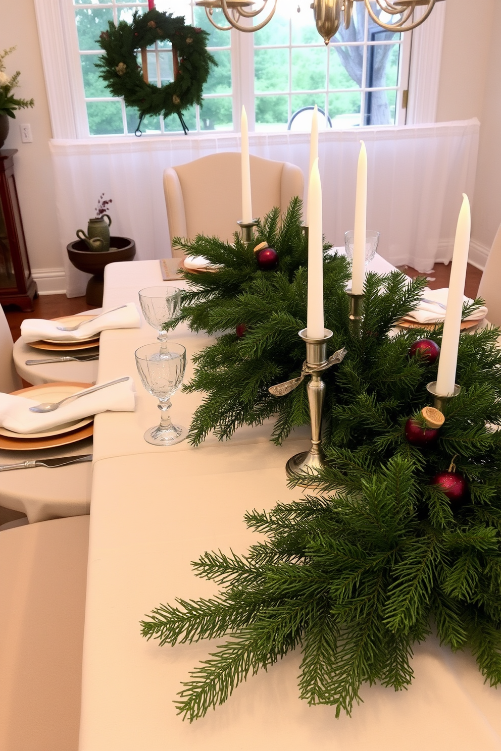 A beautifully set dining table adorned with a seasonal centerpiece featuring lush evergreen branches. The table is draped with a soft white tablecloth, and elegant dinnerware complements the rustic charm of the greenery.