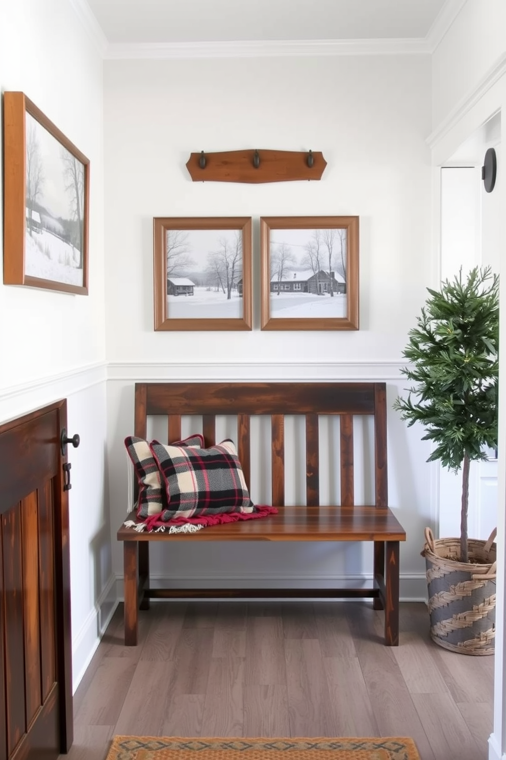 A cozy winter entryway adorned with hanging art that features serene winter scenes. The walls are painted in a soft white, and a rustic wooden bench is placed against one side, topped with a warm plaid throw.