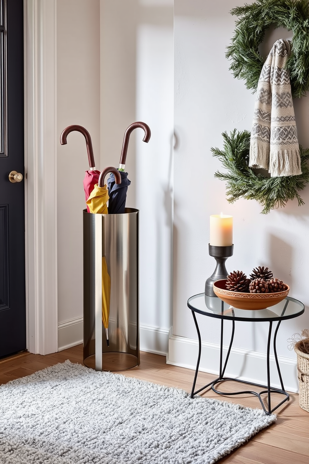 A stylish umbrella stand made of brushed metal is positioned by the door, providing a modern touch to the entryway. The stand is filled with a variety of colorful umbrellas, adding a pop of color against the neutral backdrop of the space. Cozy winter decorations adorn the entryway, including a soft wool rug in shades of grey and white. A small table beside the stand features a decorative bowl filled with pinecones and a scented candle that evokes the warmth of the season.