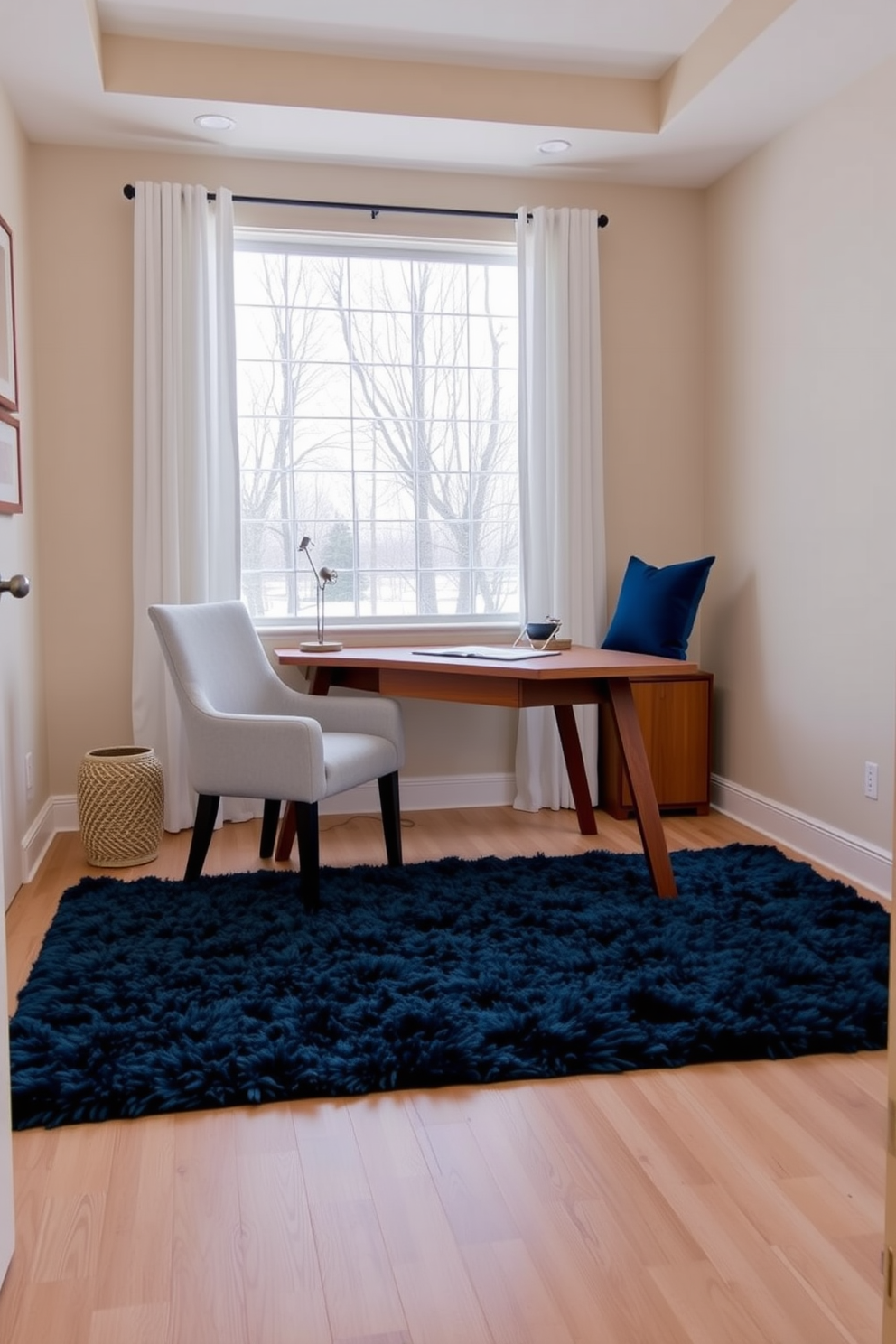 A cozy winter home office featuring a neutral color palette with pops of blue. The walls are painted in a soft beige, while a plush navy blue rug anchors the space beneath a sleek wooden desk. A comfortable chair upholstered in light gray fabric sits beside the desk, complemented by blue accent pillows. A large window allows natural light to flood the room, with sheer white curtains gently framing the view.