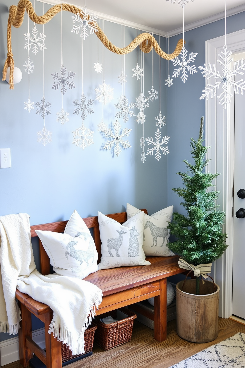 A cozy winter mudroom adorned with snowflake decorations creates a festive atmosphere. The walls are painted in a soft blue, and a rustic wooden bench is placed against one side, covered with a plush white throw. Hanging from the ceiling are delicate snowflake ornaments made of shimmering silver and white materials. A collection of winter-themed pillows is arranged on the bench, and a small evergreen tree in a decorative pot adds a touch of greenery.