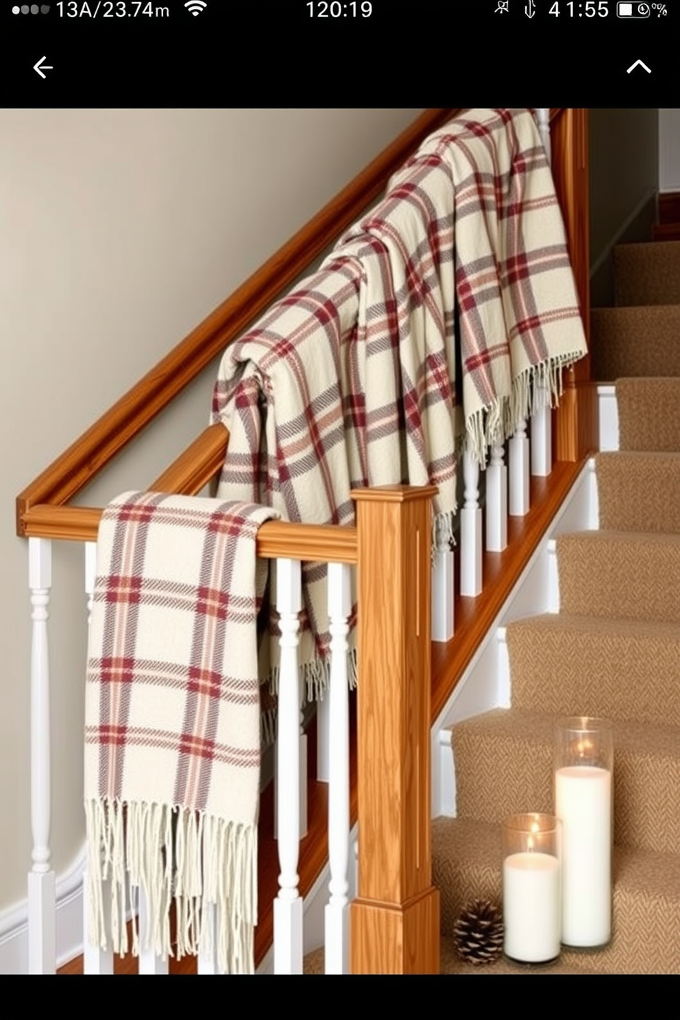 Cozy plaid blankets draped over a wooden railing create a warm and inviting atmosphere on a winter staircase. Soft, neutral-colored walls complement the rich textures of the blankets, while a few decorative pinecones and candles add a seasonal touch to the decor.